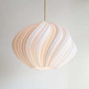 May include: A white, textured pendant light with a swirling, organic design. The light hangs from a thin, gold-coloured cord. The fixture's shape is reminiscent of a flower or a cloud, with a soft, diffused glow.