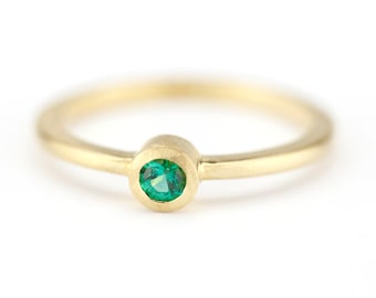 May include: A simple gold band ring with a small, round, green emerald gemstone.