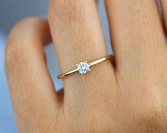 May include: A simple gold band ring with a single, small, round, clear gemstone.