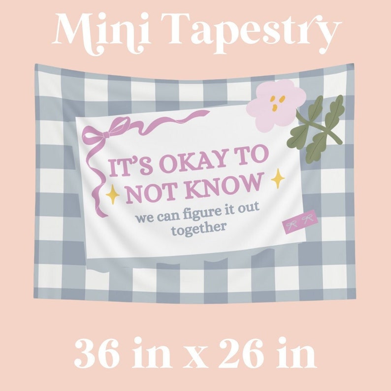 May include: A white tapestry with a blue and white checkered pattern. The tapestry features a pink and white flower, a pink ribbon, and a white rectangle with the text "IT'S OKAY TO NOT KNOW" and "we can figure it out together". The tapestry measures 36 inches by 26 inches.