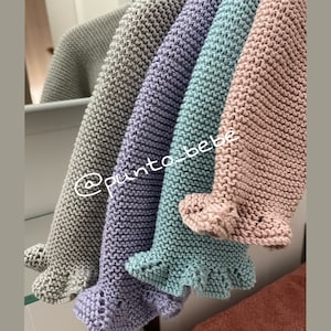 Könnte beinhalten: Vier gestrickte Babydecken in verschiedenen Farben: Grau, Lavendel, Türkis und Rosa. Jede Decke hat einen gekräuselten Rand.
