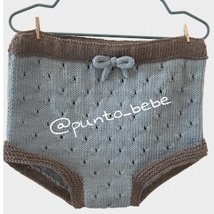 Puede incluir: Braguitas de bebé de punto azul claro con ribete marrón y un lazo en la cintura. Las braguitas tienen un delicado patrón calado. El texto '@punto_bebe' es visible en las braguitas.