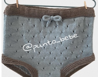 May include: Light blue knitted baby bloomers with brown trim and a bow at the waist. The bloomers have a delicate openwork pattern. The text '@punto_bebe' is visible on the bloomers.
