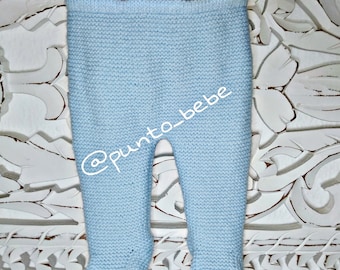 May include: Light blue knitted baby pants hanging on a clothesline. The pants have a ribbed texture and are made of a soft, comfortable material. The pants are tagged with the social media handle @punto_bebe.