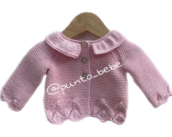 May include: A pink knitted baby cardigan with a white collar and button closure. The cardigan has a scalloped hem and is hanging on a wooden hanger.