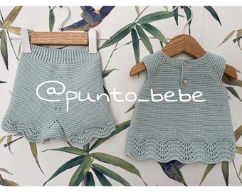 May include: A light blue knitted baby dress and matching shorts set with a scalloped hem. The set is hanging on wooden hangers against a backdrop of green bamboo leaves.