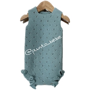 Könnte beinhalten: Ein hellblauer gestrickter Baby-Strampler mit einem zarten Lochmuster und Rüschenbesatz. Der Strampler hängt an einem Holzbügel. Der Text '@punto_bebe' ist auf dem Strampler sichtbar.