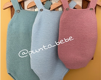 May include: Three knitted baby onesies hanging on wooden hangers. The onesies are in shades of light blue, teal, and pink. The onesies have straps and a button closure. The text '@punto_bebe' is visible on the image.