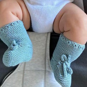 May include: A pair of light blue knitted baby booties with a bow detail. The booties are made of a soft, textured yarn and have a comfortable fit.