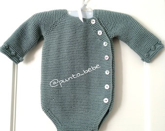 May include: A knitted baby onesie in a light blue-green color with a white button closure down the side. The onesie has a white tag with the text "@punto_bebe" on the front.