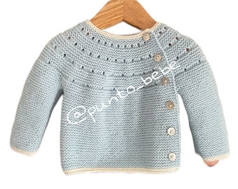 May include: A light blue knitted baby sweater with a white trim and button closure. The sweater has a delicate stitch pattern and a slightly oversized fit.