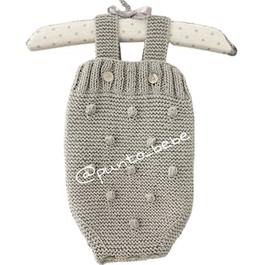 Puede incluir: Un pelele de bebé de punto gris con un patrón texturizado de pompones y dos botones. El pelele tiene tirantes que pasan por encima de los hombros.