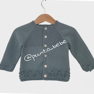 Pode incluir: Cardigã de bebê cinza-azulado de malha com mangas compridas e fecho de botões. O cardigã apresenta um padrão decorativo nos punhos e na bainha. O texto "@punto_bebe" é visível.