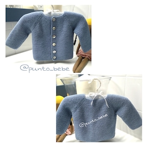 Puede incluir: Un cárdigan de punto azul claro para bebé con cierre de botones. El cárdigan se muestra en una percha y en una muñeca. El texto '@punto_bebe' es visible en la imagen.