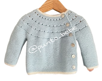 May include: A light blue knitted baby sweater with a white trim and button closure. The sweater has a delicate stitch pattern and a slightly oversized fit.