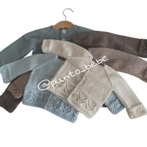 Könnte beinhalten: Vier gestrickte Baby-Cardigans in verschiedenen Farben: hellblau, beige, braun und dunkelblau. Die Cardigans haben einen Knopfverschluss und ein zartes Spitzenmuster am Saum.