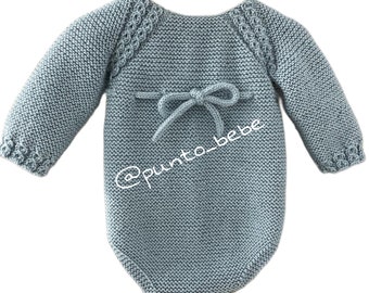May include: A light blue knitted baby onesie with long sleeves and a bow tie detail on the back. The onesie has a textured knit pattern and a @punto_bebe logo.
