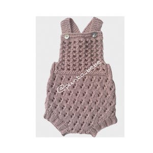 Puede incluir: Un pelele de bebé tejido de color rosa empolvado con un patrón de diamantes. El pelele presenta un diseño de cuello en V con dos pequeños botones en las correas. El texto "@punto_bebe" es visible en la prenda.