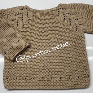 May include: A beige knitted sweater with a unique stitch pattern on the shoulders and sleeves. The sweater has a round neckline and long sleeves. The sweater is made of a soft, comfortable material.