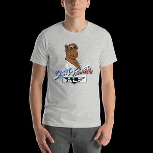 May include: A grey t-shirt with a graphic of ALF from the TV show ALF, dressed as a karate fighter. The graphic includes the text "Street Fighter" and "ALF".