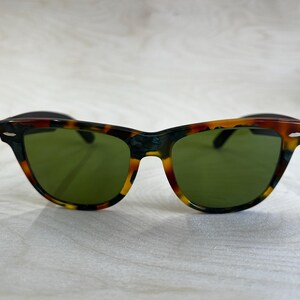 K&ouml;nnte beinhalten: Sonnenbrille mit Schildpattmuster und gr&uuml;nen Gl&auml;sern. Die Fassungen haben ein klassisches Design mit einer Mischung aus Braun-, Schwarz- und Gelbt&ouml;nen. Diese Sonnenbrille ist ein stilvolles Accessoire.