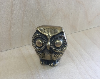 May include: A small, brass owl figurine with detailed features, including large eyes and a textured body.