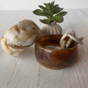 May include: Two resin bangle bracelets with a marbled finish. One bracelet features a creamy white and tan swirl pattern, while the other is a translucent amber brown. A small chain link piece in a matching cream and tan tone rests inside the amber bangle.