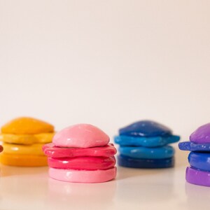 May include: A row of colourful, stacked, clay-like objects resembling miniature hamburgers. The objects are in shades of orange, pink, blue, and purple.