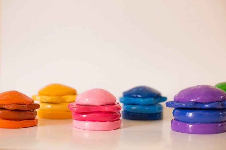 May include: A row of colourful, stacked, clay-like objects resembling miniature hamburgers. The objects are in shades of orange, pink, blue, and purple.