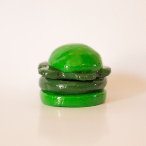 May include: A green clay sculpture of a hamburger with three layers.