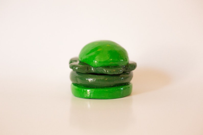 May include: A green clay sculpture of a hamburger with three layers.