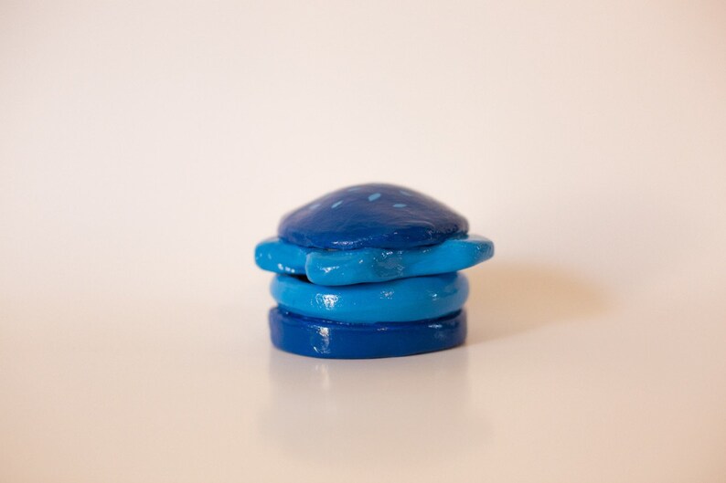 May include: A stack of four blue and teal ceramic coasters with a starburst design. The coasters are painted with a speckled pattern.