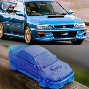 May include: A blue Subaru Impreza WRX STI with a license plate that reads "ZZB". The car is a model car and is sitting on a wooden surface.