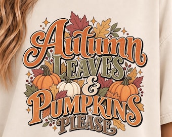 May include: A cream-colored t-shirt featuring a graphic print with the text Autumn Leaves & Pumpkins Please. The design includes orange and white pumpkins surrounded by colorful fall foliage in shades of red, yellow, and green with small star accents.