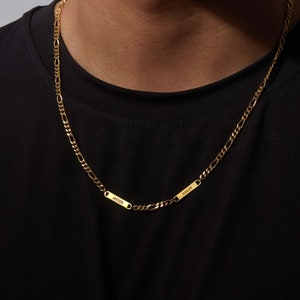Puede incluir: Collar de cadena Figaro dorado con dos placas rectangulares con nombres. Las placas con nombres est&aacute;n grabadas con los nombres "Jayden" y "Hailey". El collar se lleva sobre una camiseta negra.