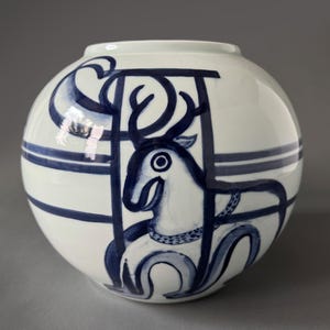 May include: A white ceramic vase with a blue and white design of a deer with antlers. The vase is round and has a smooth, glossy finish.