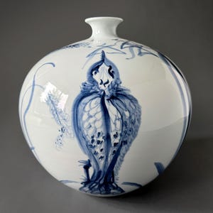 May include: A white ceramic vase with a round body and a narrow neck. The vase is decorated with a blue and white floral design, featuring a stylized bird with intricate details.