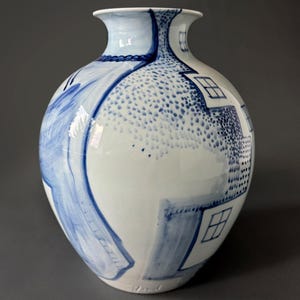 May include: A white ceramic vase with a blue and white abstract design. The vase has a rounded body and a narrow neck. The design features geometric shapes and dots.