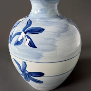 May include: A white ceramic vase with a blue and white floral design. The vase has a rounded body and a narrow neck.