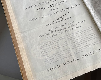 May include: An open newspaper page featuring a vintage Ford advertisement. The ad announces a $25-a-month time payment plan for a new Ford V-8 car. The text includes details about financing and insurance.