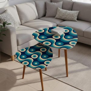 Pode incluir: Duas mesas laterais retrô em forma de gota. As mesas apresentam um fundo azul escuro com um padrão de círculos turquesa, azul claro e bege. Possuem pernas de madeira e estão colocadas em frente a um sofá cinza.
