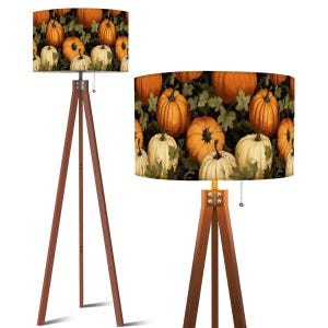 May include: Two wooden tripod floor lamps. The lampshades feature a repeating pattern of orange and white pumpkins against a dark green background. The wooden legs are a dark brown color.