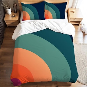 Puede incluir: Juego de cama con funda nórdica y dos fundas de almohada. El diseño presenta un patrón semicircular de inspiración retro en tonos turquesa, naranja y azul marino. La funda nórdica y las fundas de almohada están sobre una colcha blanca.