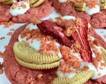 May include: Three pink sugar cookies topped with white frosting, crushed red candy, and Oreo cookies. Dried strawberries are on top of the cookies. The cookies are on a white surface. The text "Tabitha Bakes" is in the bottom right corner of the image.