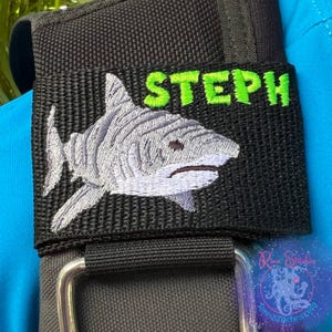 May include: Black adjustable strap with a white embroidered shark and green embroidered text that says "STEPH".