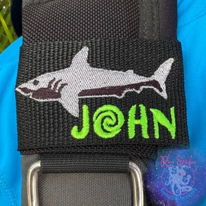 Pode incluir: Correia ajustável preta com um tubarão bordado em branco e cinza e um texto bordado em verde que diz "JOHN".