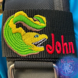 May include: A black and green embroidered patch with a yellow moray eel design and the name "John" in red embroidery.