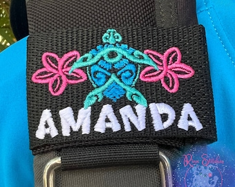May include: Black fabric strap with a pink and blue embroidered turtle design and the name Amanda in white lettering.