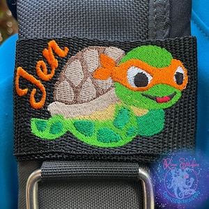 May include: A black fabric bag with a green and orange embroidered turtle design and the name "Jen" embroidered in orange thread.