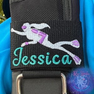 May include: A black fabric patch with a white silhouette of a scuba diver with purple accents. The name "Jessica" is embroidered in teal below the diver.